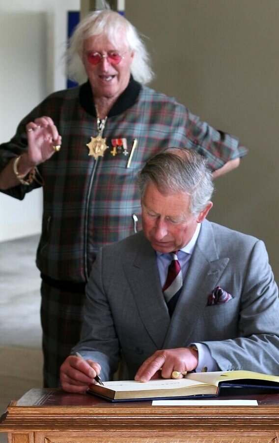 Jimmy-Savile-mimics-Prince-Charles-as-he-signs-a-book-during-his-visit-to-Rotunda-Museum-in-Scarborough-4009249.jpg